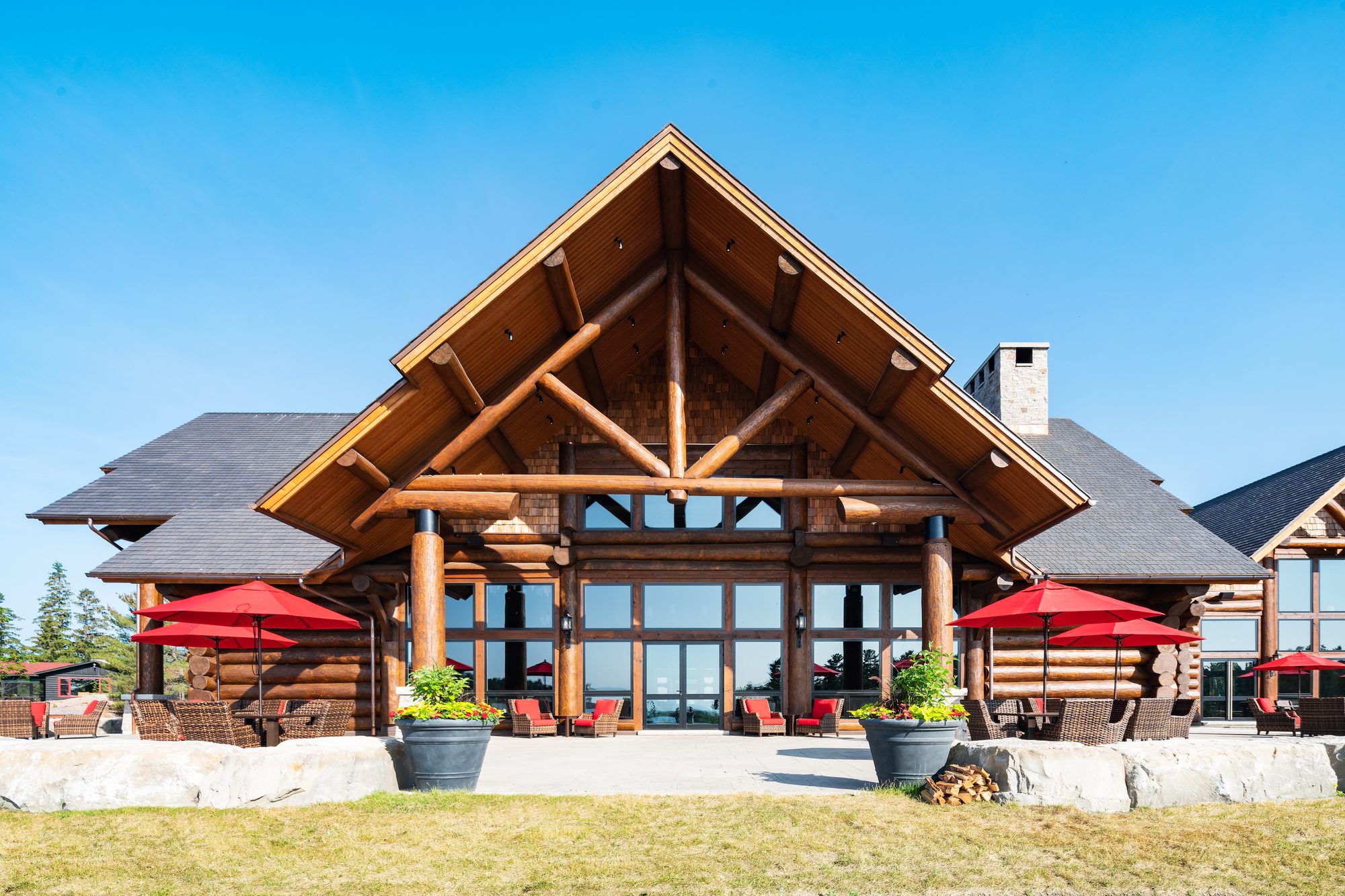 The lodge's log-and-glass gable above a stone terrace with red umbrellas