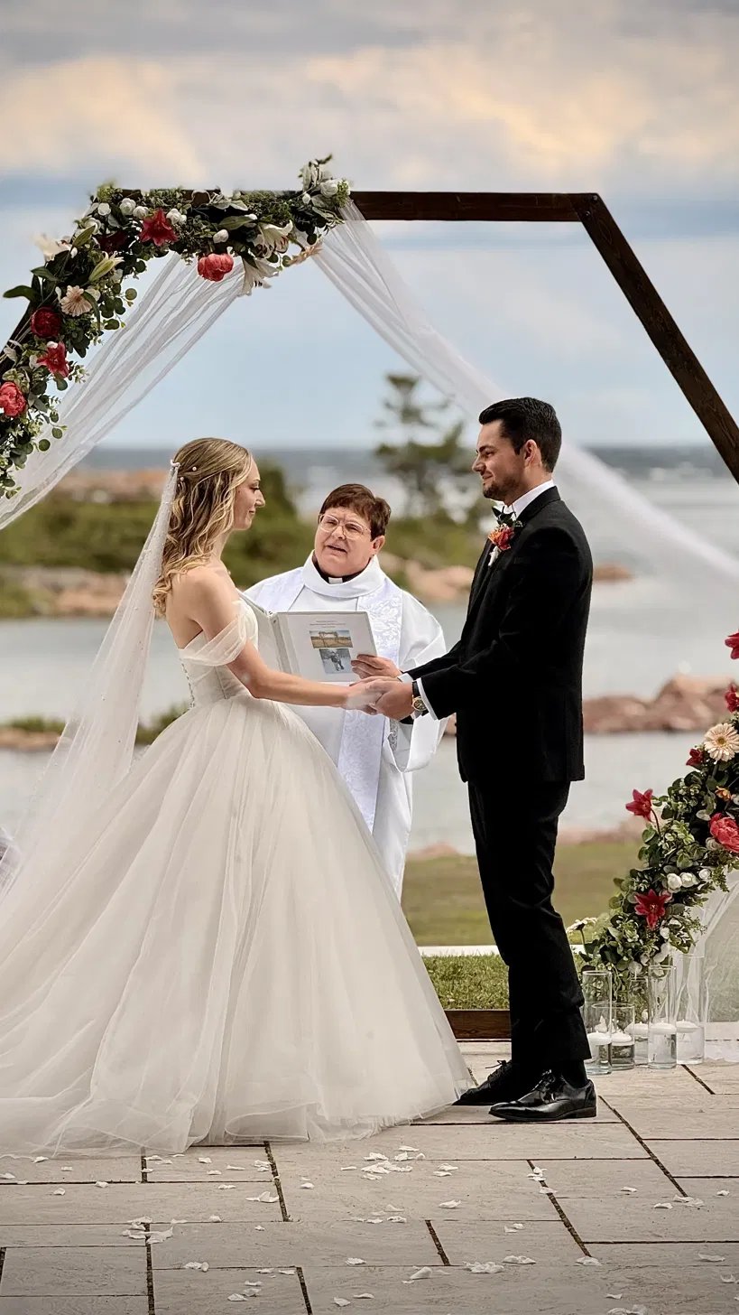 Couple exchanging vows beneath a hexagonal floral arch with Georgian Bay behind