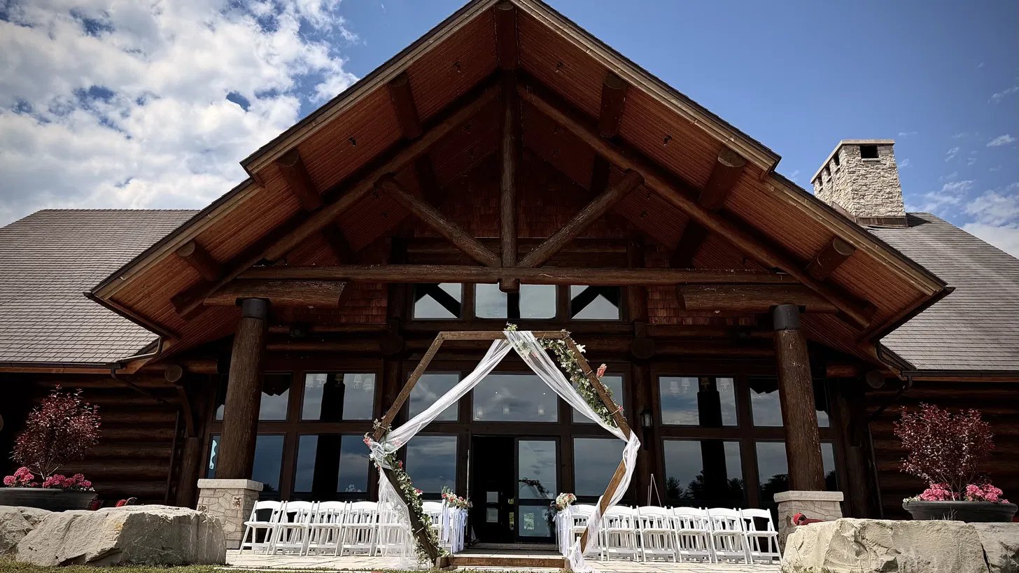 A floral arch and white ceremony chairs before the great log gable