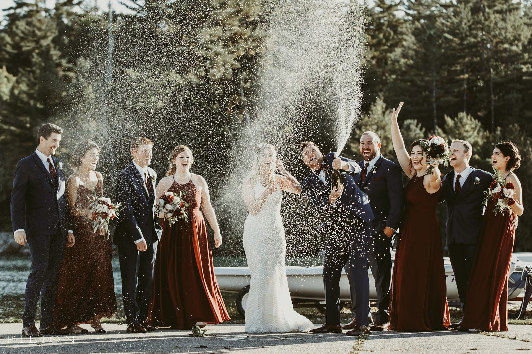 Wedding party cheering through a champagne spray by the water