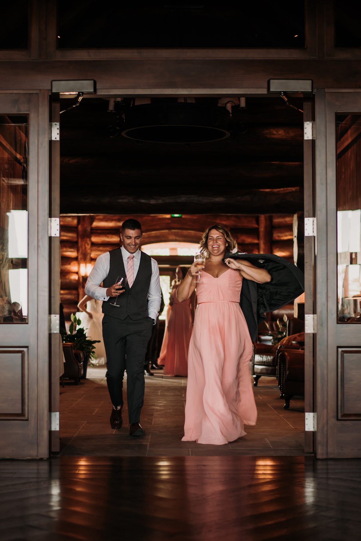 Guests arriving through the timber doorway into the warm log-lit lobby, drinks in hand